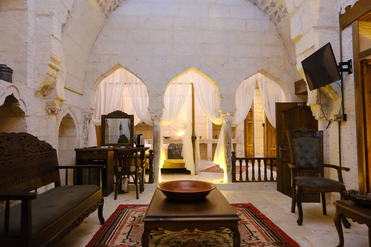 A room with a wooden table, a bench, and a chair. There are arches in the background and a door labeled 107.