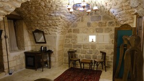 Une pièce aux murs de pierre, avec une table en bois, des chaises, un miroir et un lustre.