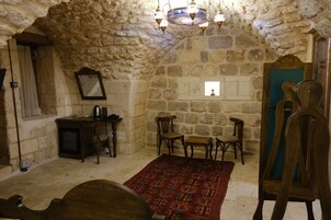 Una habitación con paredes de piedra, una mesa de madera, sillas, un espejo y una araña.