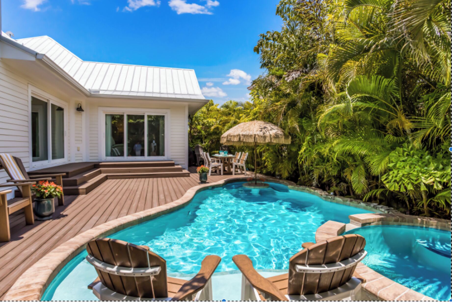 A pool area with wooden deck, lounge chairs, and a house with a white exterior.