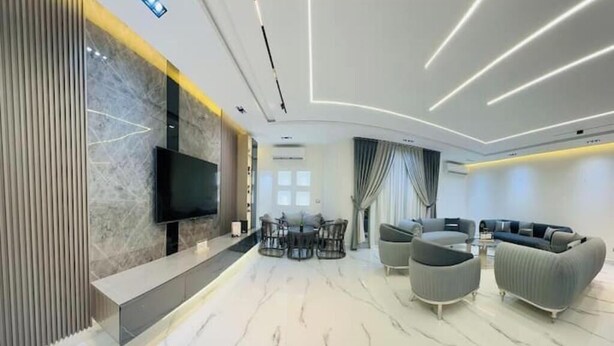 Uma sala de estar moderna com televisão de tela plana, piso de mármore e móveis contemporâneos.