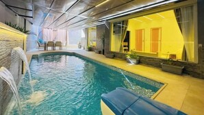 An indoor swimming pool with a waterfall feature, stone walls, and a seating area with chairs and a table. - Lux privat hjem Sheikh zayed (Second Al Sheikh Zayed)