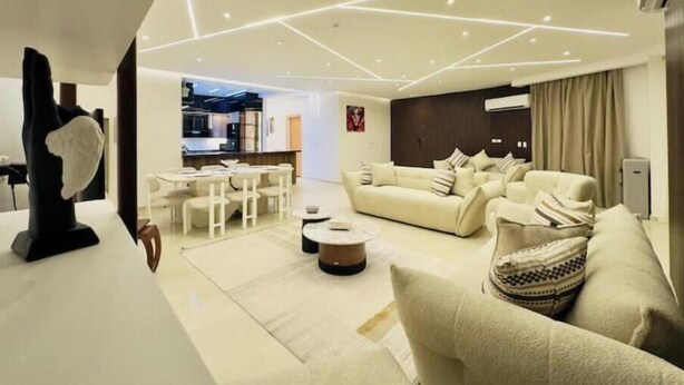 A modern living room with a sofa, coffee table, and a dining area with chairs. - Lux privat hjem Sheikh zayed (Second Al Sheikh Zayed)