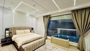 A modern bedroom with a large bed, a bench, a view of a pool, and a ceiling with recessed lighting. - Lux privat hjem Sheikh zayed (Second Al Sheikh Zayed)