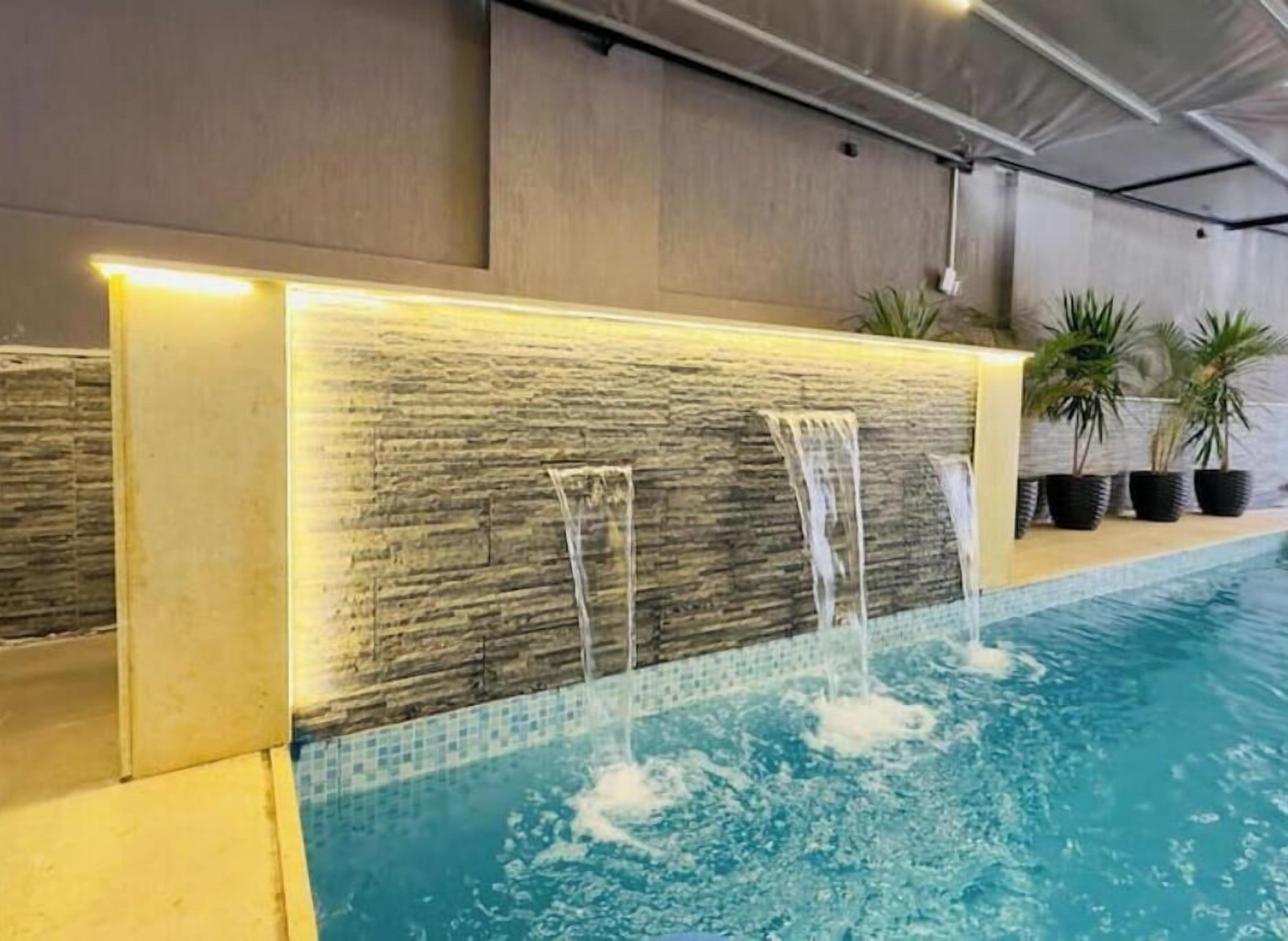 A pool with a waterfall feature and potted plants along the edge.