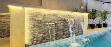 A pool with a waterfall feature and potted plants along the edge.