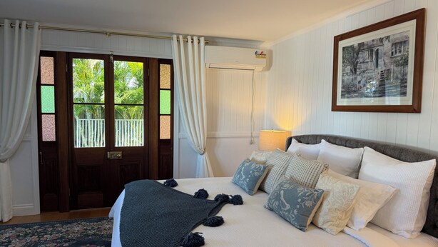 A bedroom with a bed, a nightstand, a lamp, a framed picture on the wall, and a door with a view of greenery outside.
