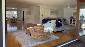 A spacious living room with a large wicker chair, a sofa with a blue blanket, and a dining area with a table and chairs.