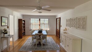 A dining area with a table, chairs, a ceiling fan, a window with blinds, a bookshelf, and a cabinet with decorative items.