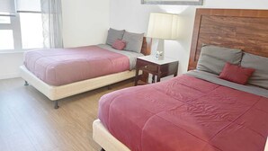 Habitación de hotel con dos camas, un escritorio, una lámpara y una ventana con cortinas.