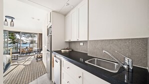 A modern kitchen with white cabinets, a black countertop, and a stainless steel sink. - The Manly Wave Beachfront Ocean Views (Manly)