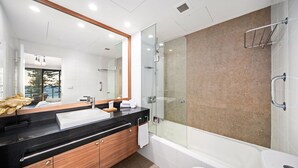 A modern bathroom with a glass-enclosed shower, a large mirror, and a black countertop with a white sink. - The Manly Wave Beachfront Ocean Views (Manly)