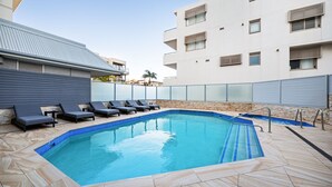 A swimming pool with lounge chairs, a stone-tiled deck, and a modern building with balconies. - The Manly Wave Beachfront Ocean Views (Manly)