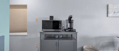 A compact kitchen with a microwave, coffee maker, and a small cabinet.