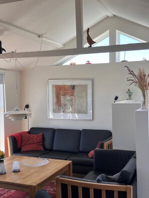 A modern living room with a black sofa, a wooden coffee table, and a framed abstract painting on the wall.