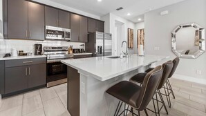 Une cuisine moderne avec des meubles de couleur sombre, des appareils en acier inoxydable, un grand îlot central doté de tabourets de bar et un miroir décoratif au mur.