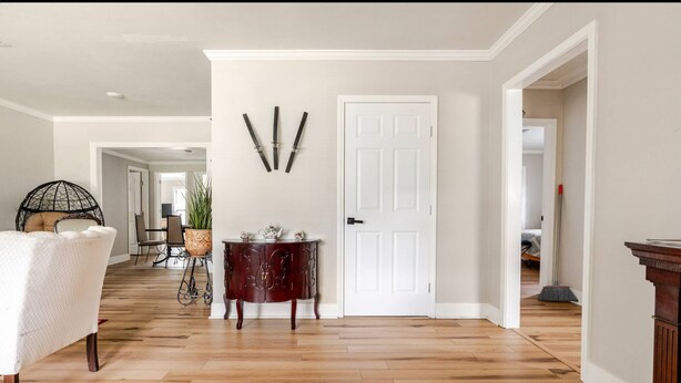 Una habitación amplia con piso de madera, una puerta blanca y una zona de comedor con una mesa y sillas.