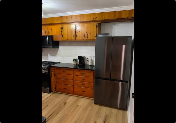 A kitchen with wooden cabinets, a stainless steel refrigerator, a stove, and a countertop with various appliances. - Charming 3-bedroom house with AC in lovely Hammond (Hammond)