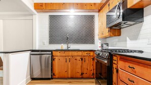 Una cocina con gabinetes de madera, lavavajillas de acero inoxidable y estufa negra.