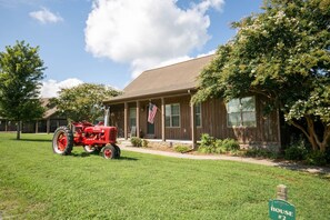 Una casa de un piso con un porche delantero, una bandera estadounidense y un tractor rojo estacionado en el jardín.