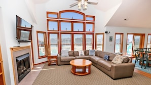 A spacious living room with a sectional sofa, a fireplace, a television, and large windows offering a view of the city. - Semi-Oceanfront, Priv Pool, Hot Tub, ELEV, Rec Rm-WL980, OBX Beach Bliss (Corolla)
