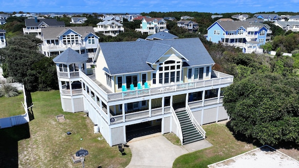 A large, two-story house with a balcony and a covered porch, surrounded by other houses. - Semi-Oceanfront, Priv Pool, Hot Tub, ELEV, Rec Rm-WL980, OBX Beach Bliss (Corolla)