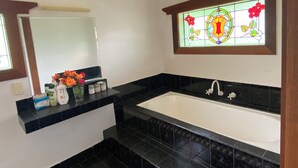 A bathroom with a white bathtub, black tiled floor, a mirror, and a stained glass window above the sink. - Pink Lakes Quairading (Quairading)
