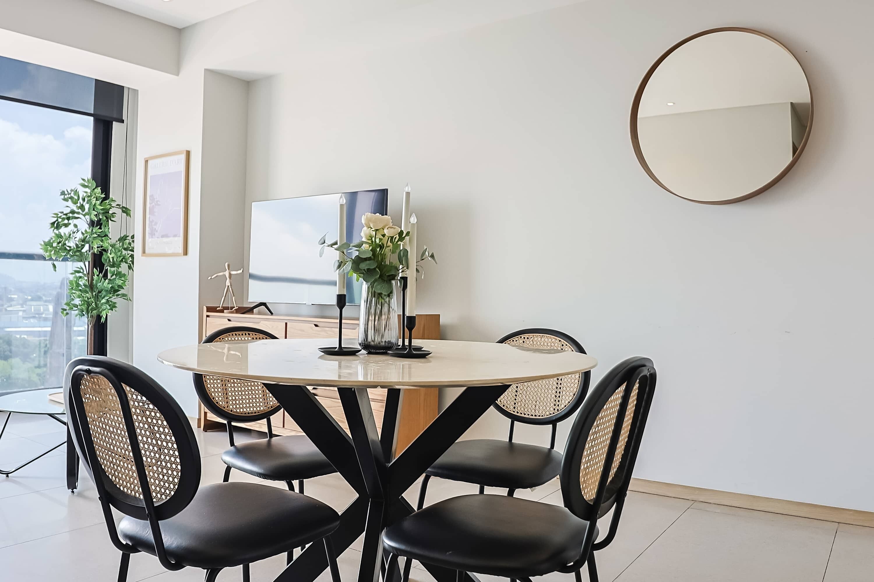 Uma sala de jantar moderna com uma mesa redonda, cadeiras pretas e um vaso com flores.