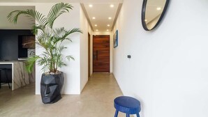 Ein modernes Interieur mit einem Flur, der zu einer Holztür führt, einer Topfpflanze, einem blauen Hocker und einem an der Wand befestigten Spiegel.