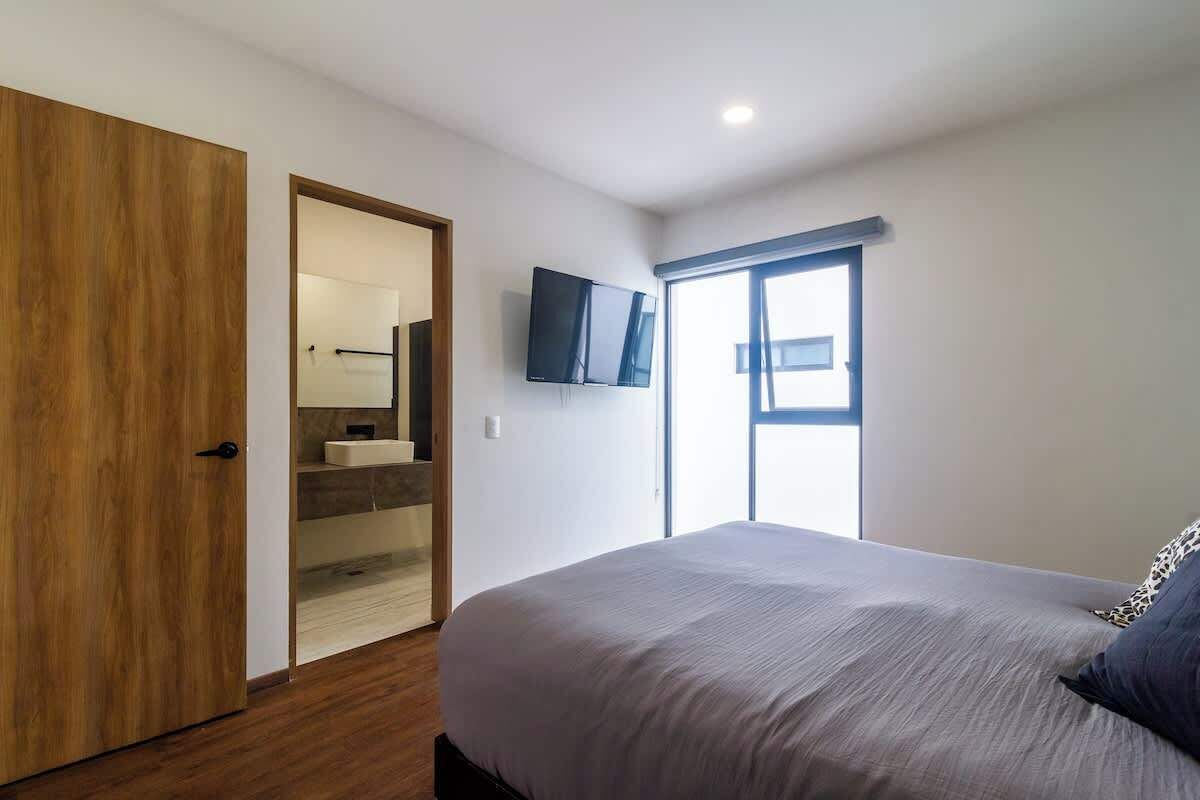 Una camera da letto con un letto, una televisione montata a parete, una finestra e una porta in legno.