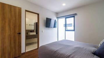 Una camera da letto con un letto, una televisione montata a parete, una finestra e una porta in legno.