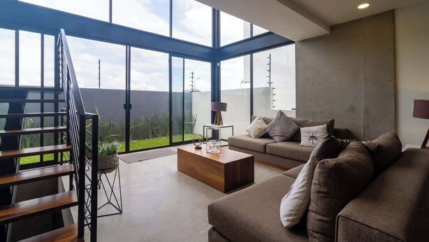 Ein modernes Wohnzimmer mit großem Fenster, einer Couch, einem Couchtisch und einer Treppe.