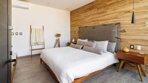 A modern bedroom with a wooden headboard, a large bed with white bedding, a bedside table with a lamp, and a wooden floor. - Rooftop Depa (Zapopan)