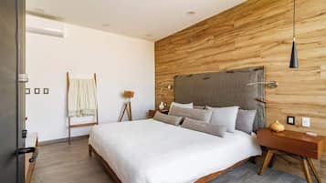 A modern bedroom with a wooden headboard, a large bed with white bedding, a bedside table with a lamp, and a wooden floor.