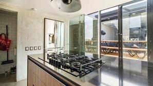 A modern kitchen with a gas stove, a large mirror, and a glass door leading to a dining area. - Rooftop Depa (Zapopan)