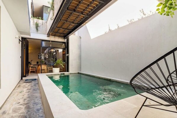 Un espace piscine extérieur moderne offrant une vue dégagée sur le bassin, un coin salon avec une table et des chaises, ainsi qu’un fauteuil suspendu.