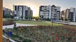 Et boligområde med moderne lejlighedskomplekser, en grøn park og en lille have med røde blomster.