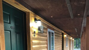 A row of log cabin-style rooms with a green door, numbered room signs, and a covered walkway. - Evergreen Escape 1 bed cabin near Tippy Dam, Trails, Lake Mi, Manistee River NEW (Wellston)