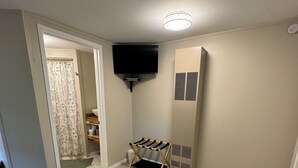 A bedroom with a bed, a TV mounted on the wall, a radiator, and a door leading to another room. - Evergreen Escape 1 bed cabin near Tippy Dam, Trails, Lake Mi, Manistee River NEW (Wellston)