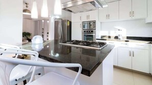 A modern kitchen with white cabinets, stainless steel appliances, and a central island with seating. - La casa de mi tia divorciada Family (Zapopan)