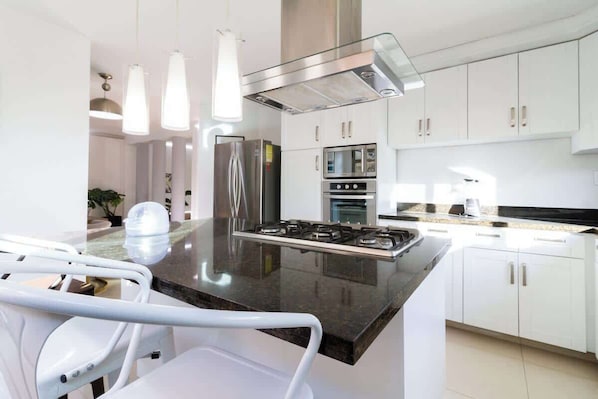 Una cocina moderna con armarios blancos, electrodomésticos de acero inoxidable y una isla central con asientos.