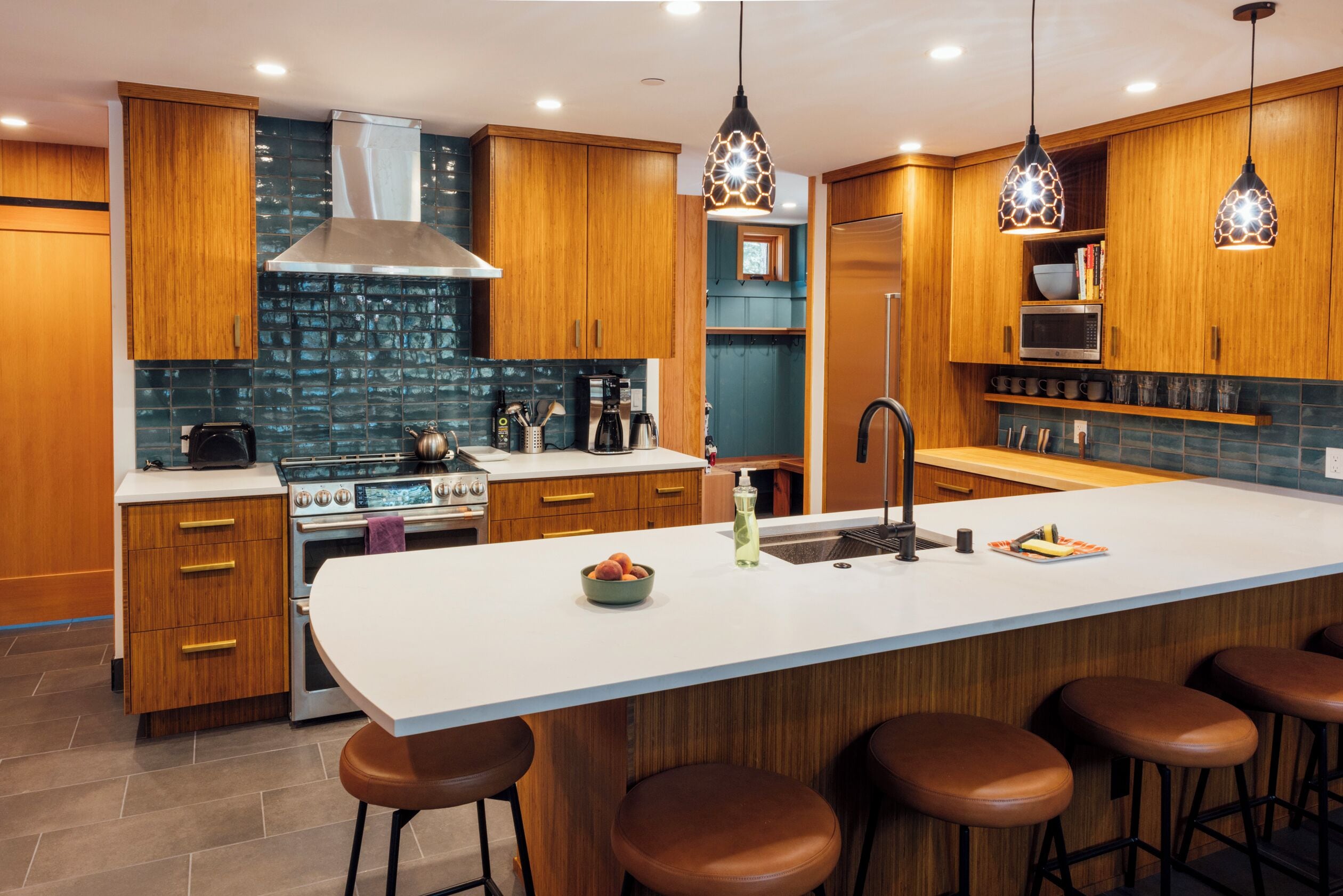 A modern kitchen with wooden cabinets, a large island with stools, a stove, and pendant lighting.