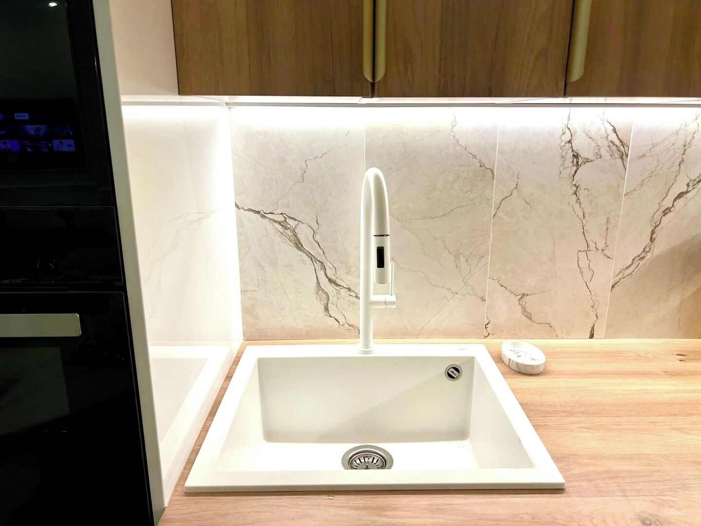 Eine Küche mit einem weißen Spülbecken, einem modernen Wasserhahn und einer Marmor-Spritzschutzwand.