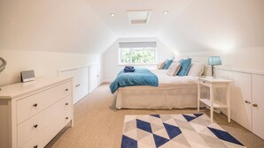 Une chambre à coucher comprenant un lit, un bureau, une commode et une fenêtre donnant sur un paysage verdoyant.