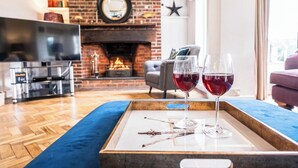 Un salon avec une cheminée en briques, un téléviseur à écran plat et deux verres de vin rouge posés sur un plateau.