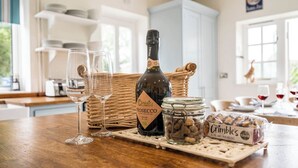 Un comptoir de cuisine avec une bouteille de Prosecco, deux verres à vin, un panier en osier, un bocal de noix et une boîte de macarons au chocolat.