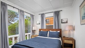 Een slaapkamer met een groot bed, twee nachtkastjes, een raam met gordijnen en uitzicht op groen.