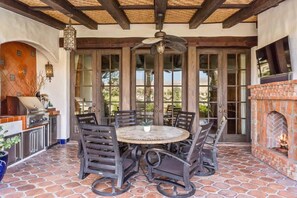 An outdoor patio with a round table and chairs, a brick fireplace, and a TV mounted on the wall. - Lakefront home w/ beach + dock (Indio)