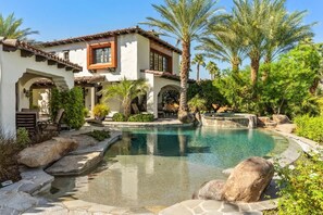 A Mediterranean-style villa with a swimming pool, palm trees, and a stone pathway. - Lakefront home w/ beach + dock (Indio)