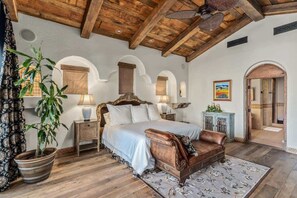 A bedroom with a wooden ceiling, a bed with a headboard, a nightstand, a potted plant, a chair, and a painting on the wall. - Lakefront home w/ beach + dock (Indio)